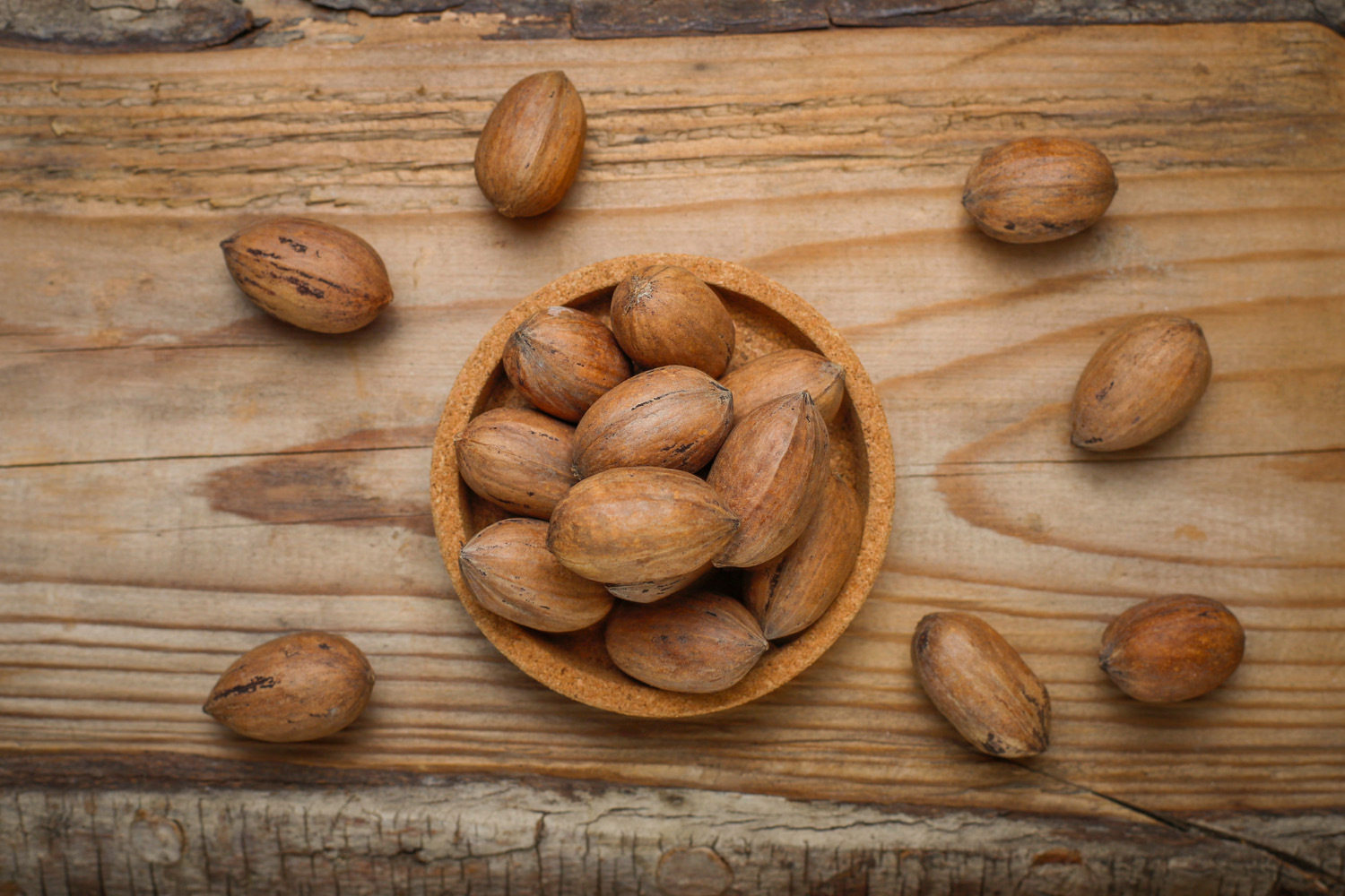 Cuenco de madera con nueces pecanas BIO con cáscara sobre una mesa rústica, resaltando la calidad y producción sostenible de Biopecans El Tesorillo S.L.